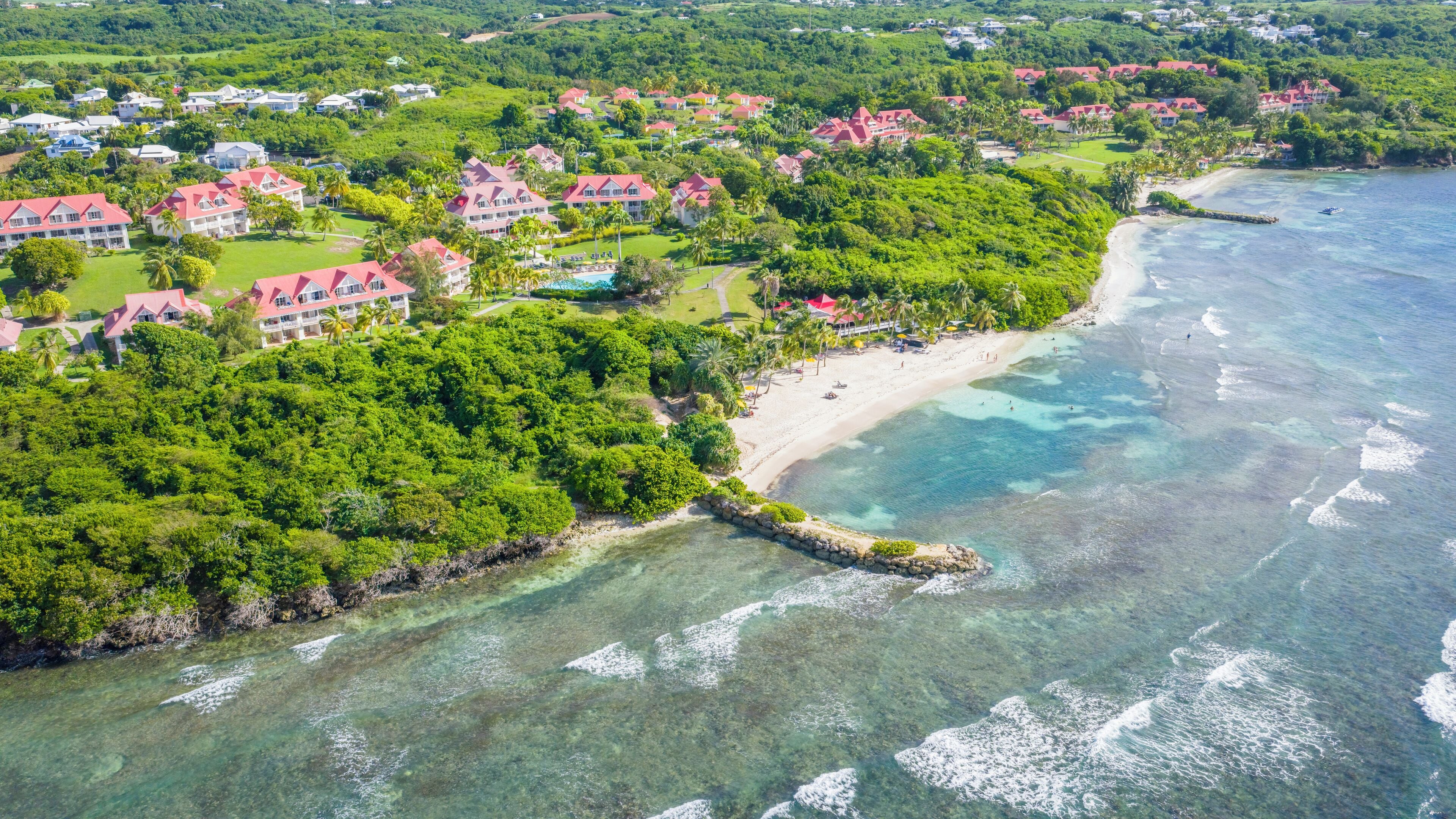 An aerial view of a coastal resort with multiple buildings, a beach, and clear waters.