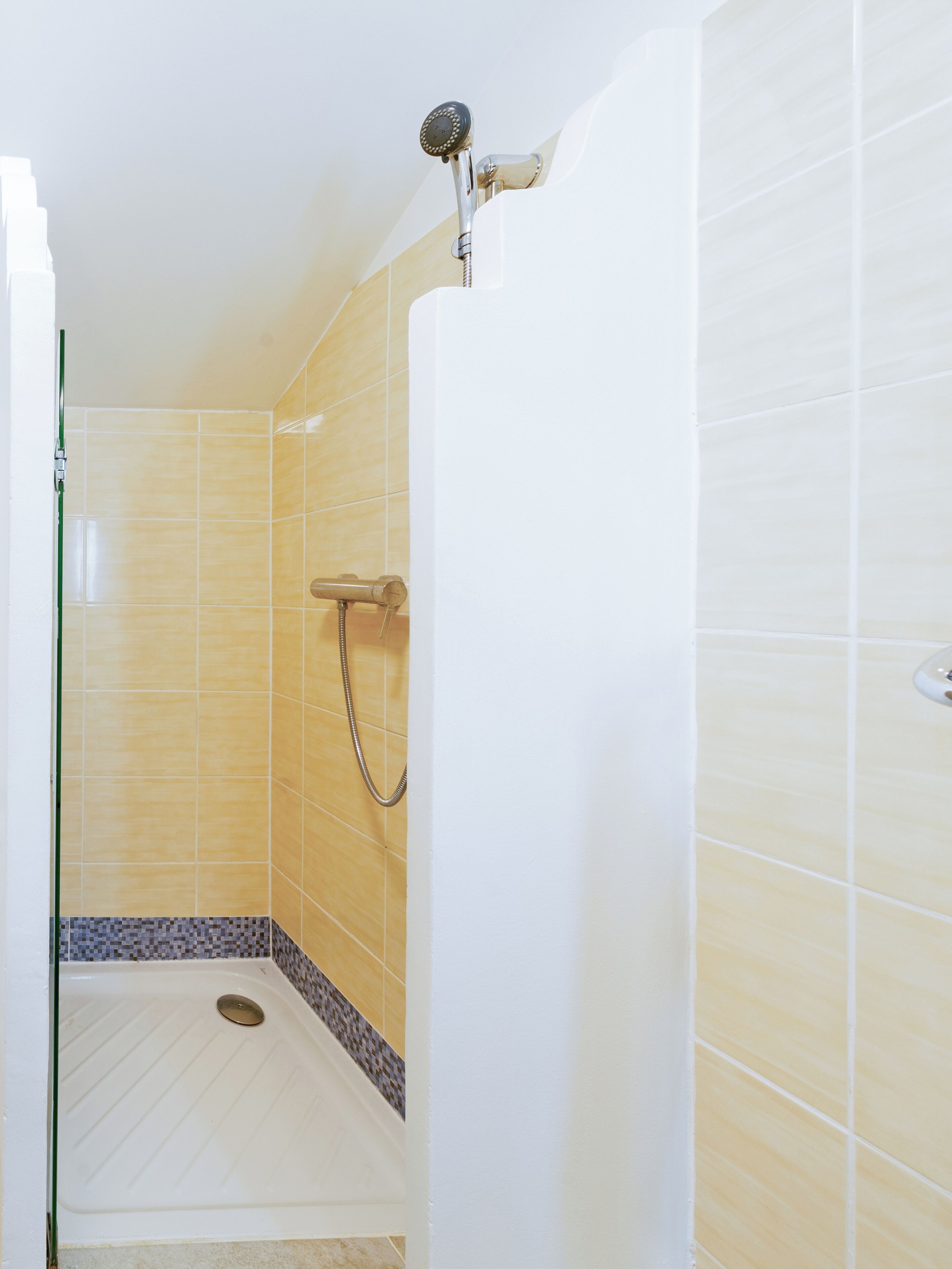 Un petit espace douche fermé, avec des carreaux jaunes et un lavabo blanc.