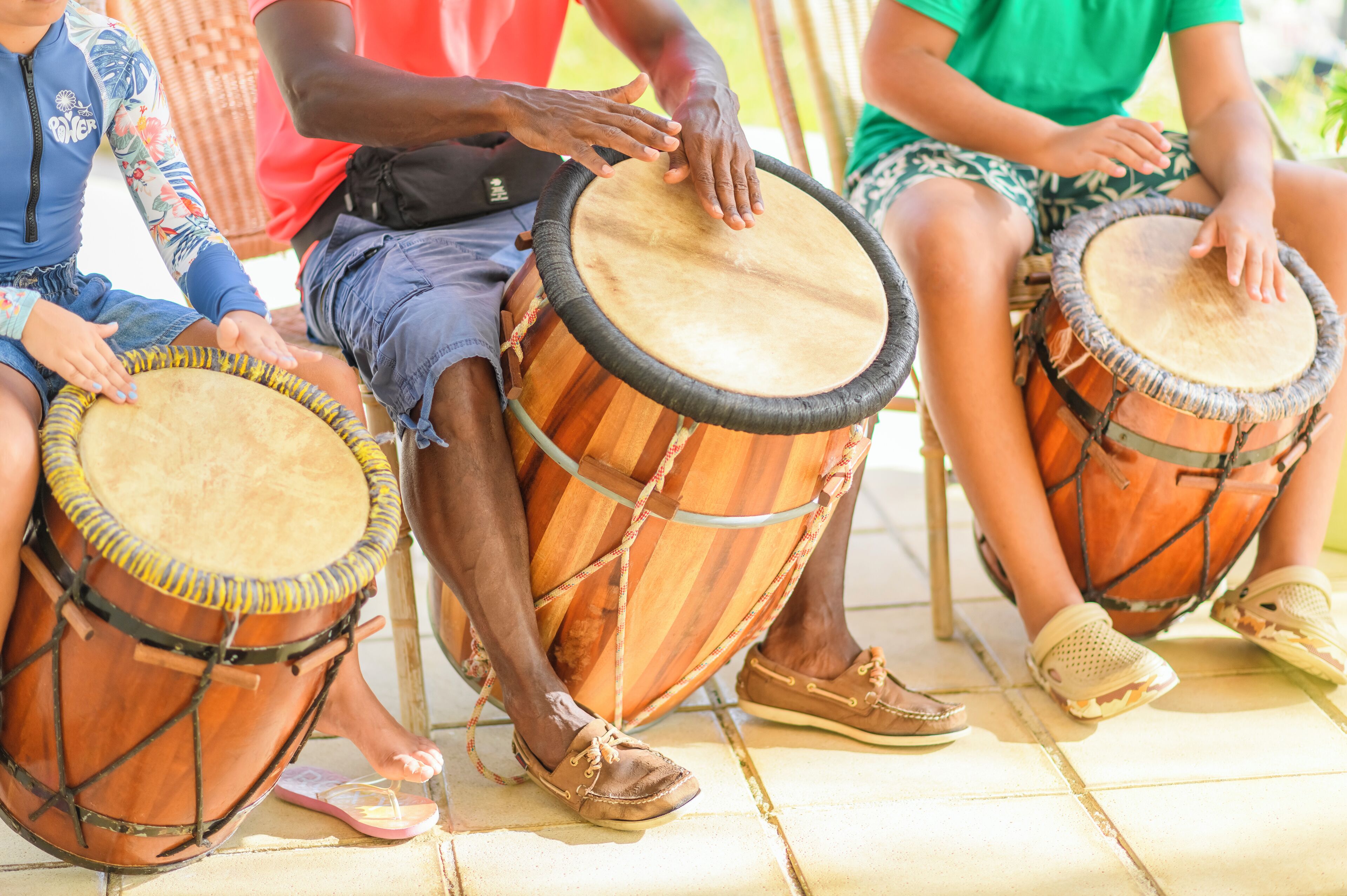Three individuals seated on a tiled floor, each playing a drum.