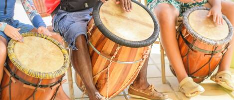 Three individuals seated on a tiled floor, each playing a drum.