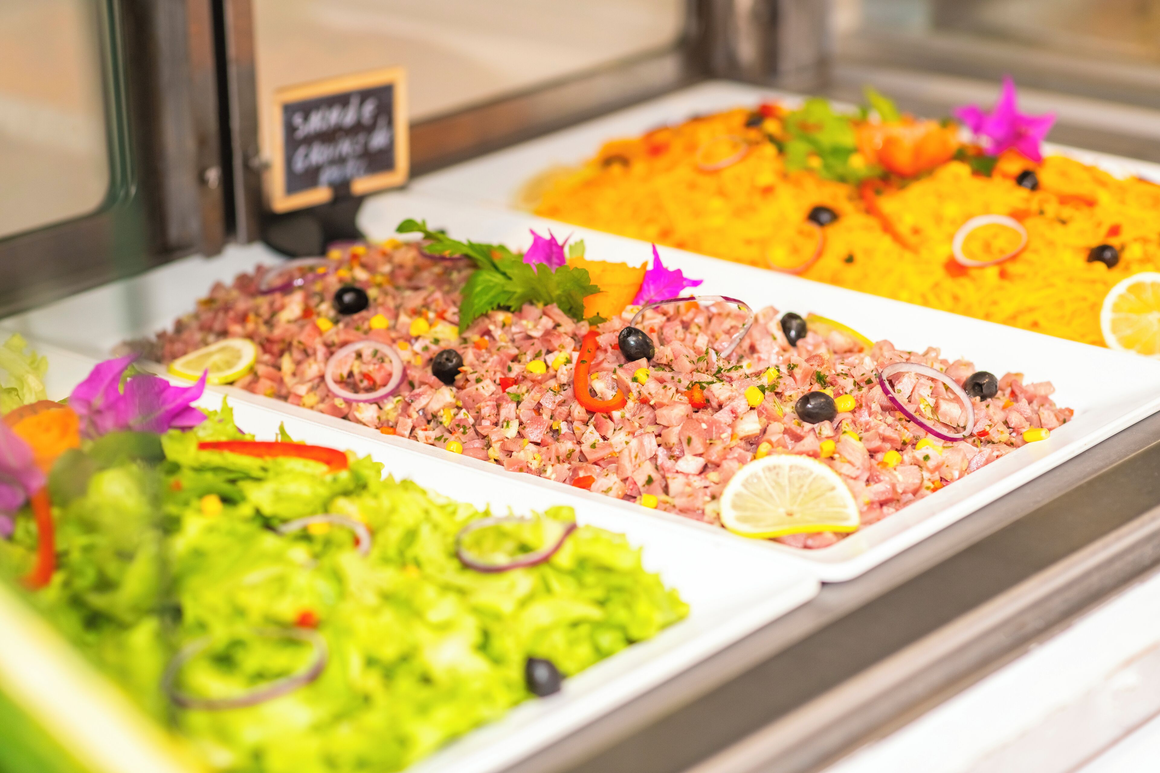 A buffet with various dishes, including a green salad, a pinkish dish with olives, and a yellow rice dish.