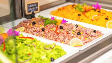 A buffet with various dishes, including a green salad, a pinkish dish with olives, and a yellow rice dish.