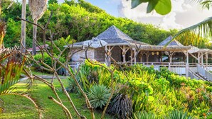 A rustic wooden building with a thatched roof, surrounded by lush greenery and tropical plants. - Village St Anne Pierre & Vacances (Sainte-Anne)