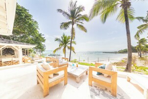 Un área de descanso frente a la playa con muebles de madera, una mesa de mármol y vistas al océano.