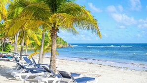 A beach with white lounge chairs and palm trees. - Village St Anne Pierre & Vacances (Sainte-Anne)