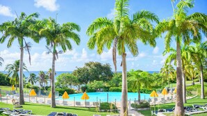 A pool area with palm trees, lounge chairs, and umbrellas. - Village St Anne Pierre & Vacances (Sainte-Anne)