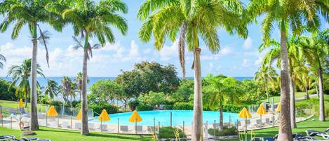 A pool area with palm trees, lounge chairs, and umbrellas.