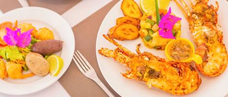A table with plates of seafood and vegetables, a fork, and a glass of orange juice.