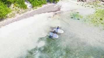 Vista aérea de una playa con aguas poco profundas y cristalinas, y una orilla arenosa.