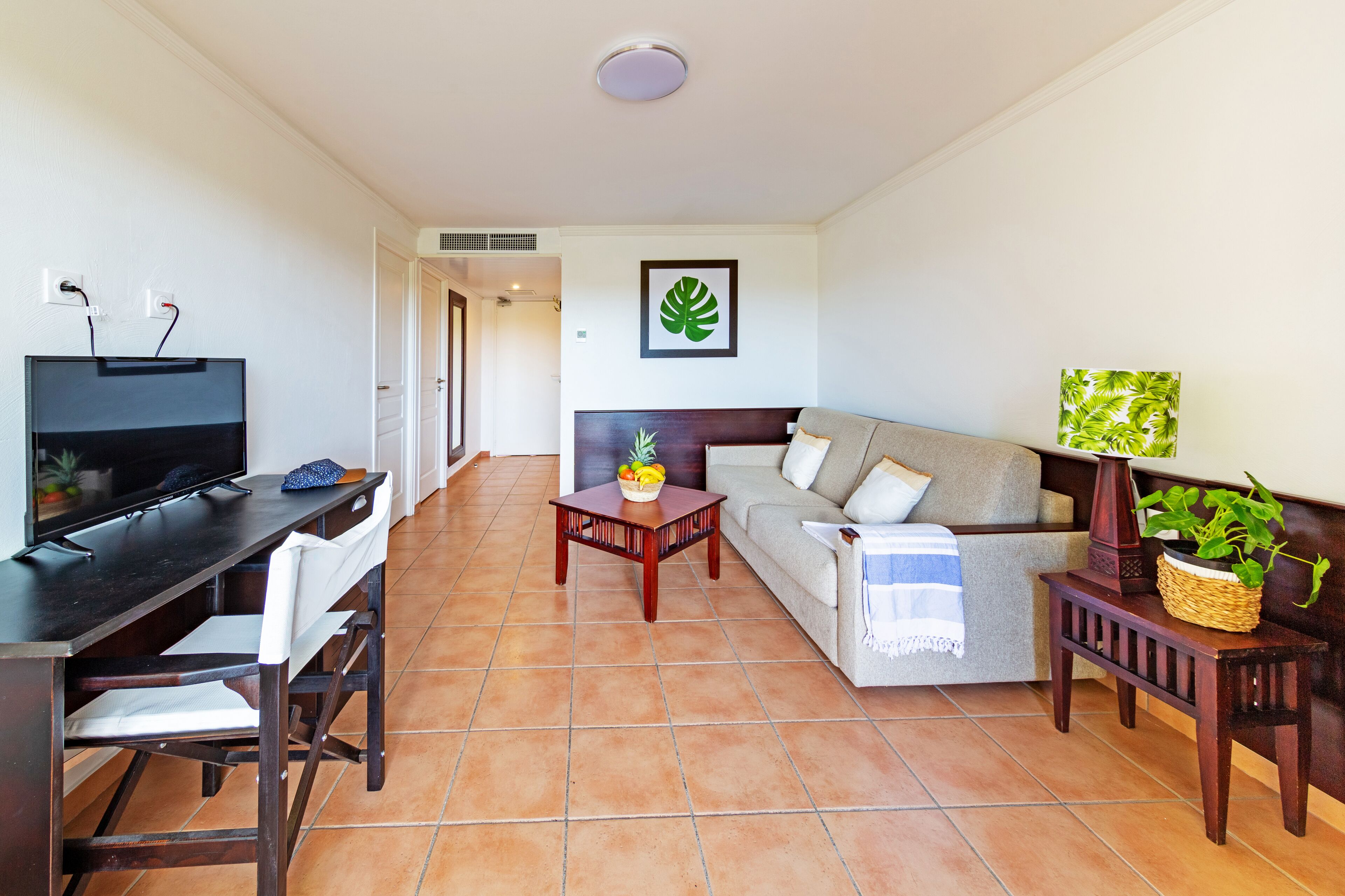 A living room with a TV, a sofa, a coffee table, and a dining area with chairs.