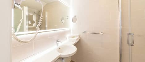 A modern bathroom with a white sink, a mirror, a hairdryer, and a glass shower enclosure.
