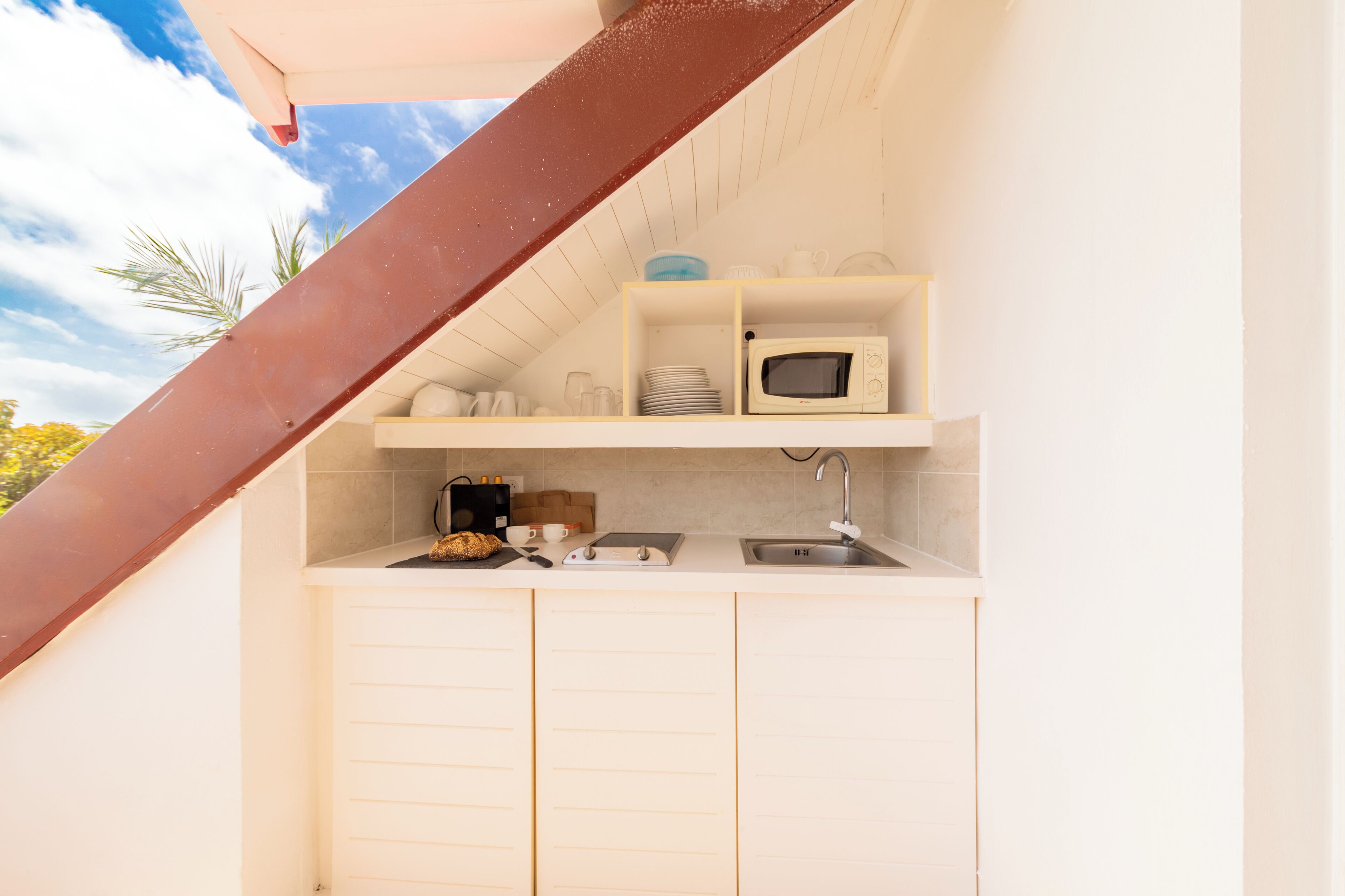 A compact kitchen with a microwave, sink, and storage shelves.