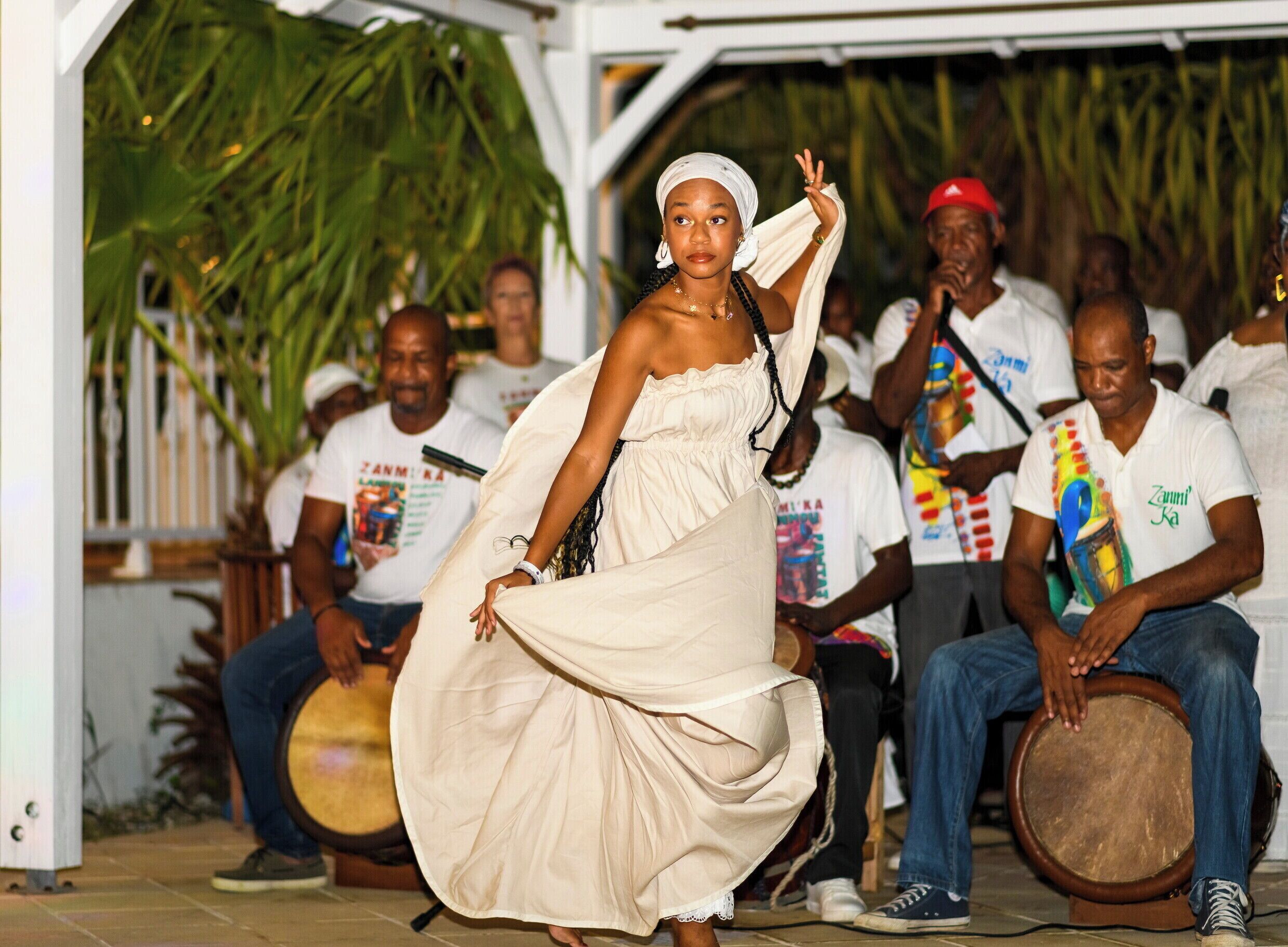 A person in a white dress dancing in front of a seated audience.