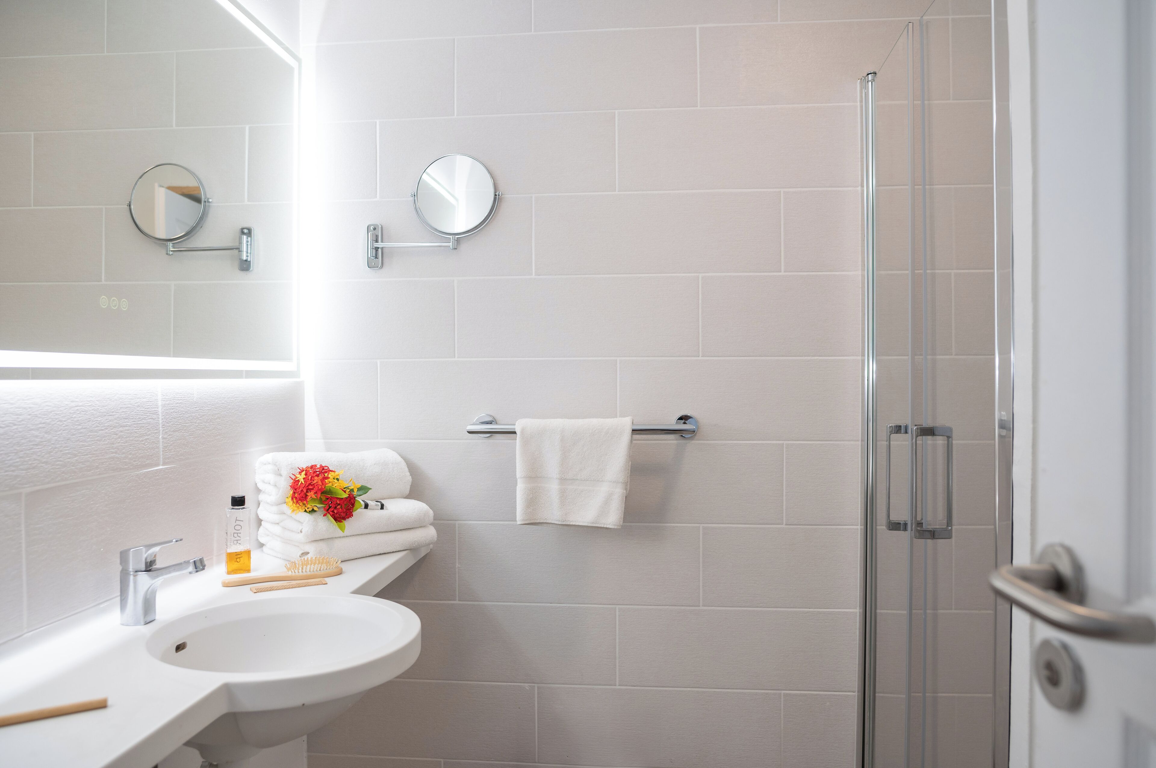 Un baño moderno con lavamanos, espejos, toallero y cabina de ducha de vidrio.