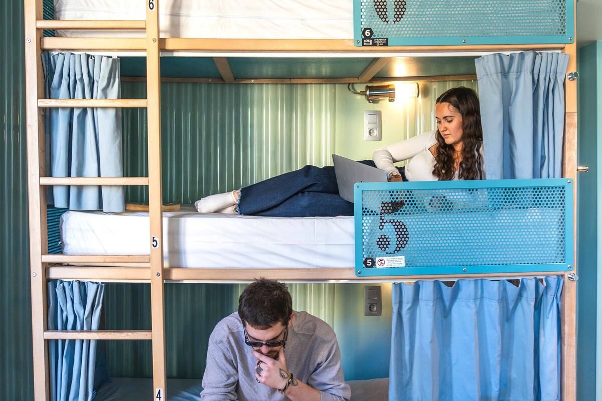 Une chambre avec des lits superposés à trois niveaux, chacun étant identifié par un numéro indiquant sa position. Une échelle se trouve sur le côté gauche, et un rideau bleu sur le côté droit.