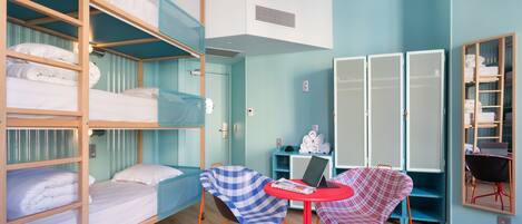Una habitación tipo dormitorio con literas, una pequeña mesa con una computadora portátil y una silla.