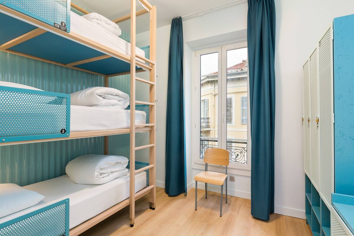 Une chambre de dortoir avec des lits superposés, une chaise et une fenêtre avec des rideaux.