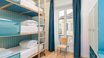 Une chambre de dortoir avec des lits superposés, une chaise et une fenêtre avec des rideaux.