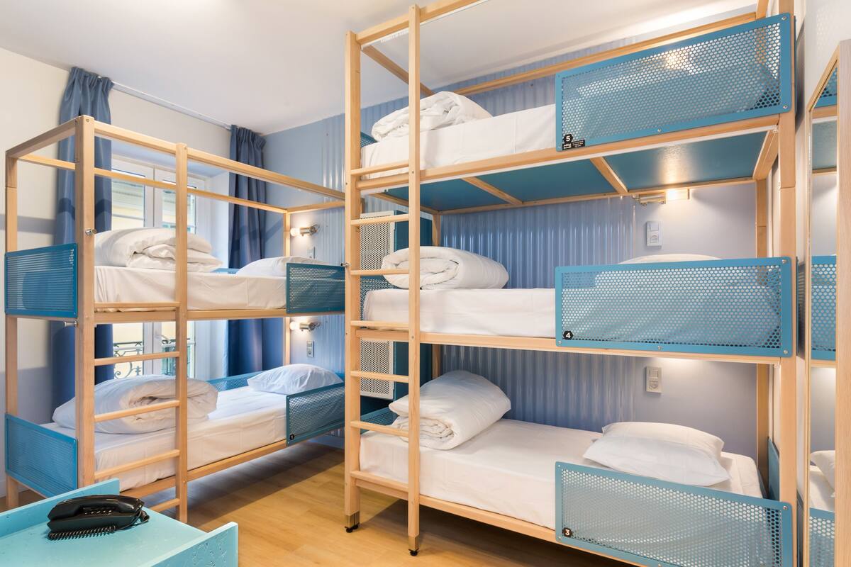 Une chambre de dortoir avec des lits superposés, un bureau avec un téléphone et une fenêtre avec des rideaux.