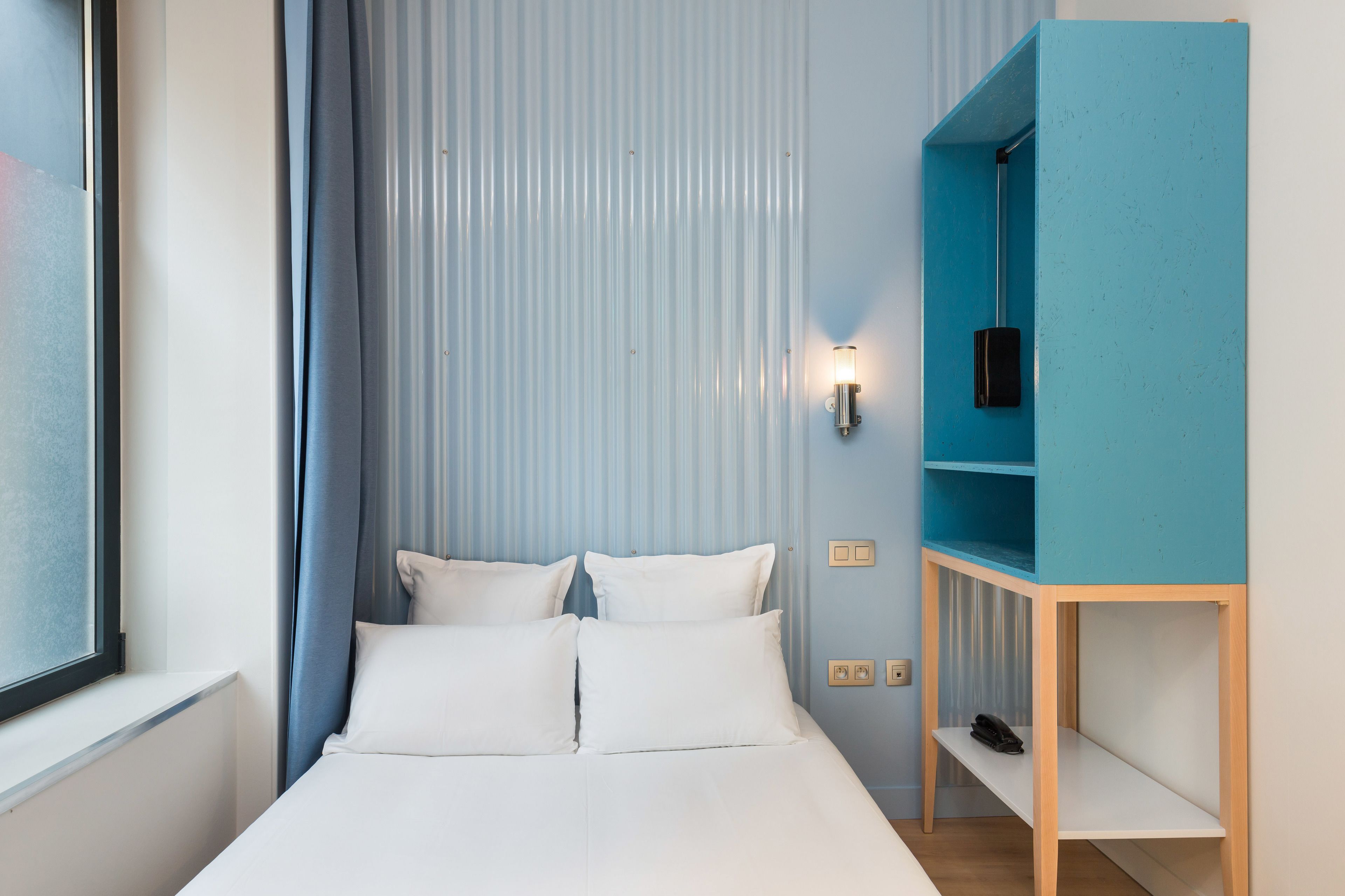 Ein ordentlich eingerichtetes Hotelzimmer mit einem Bett, einer blauen Wandverkleidung und einem Fenster.