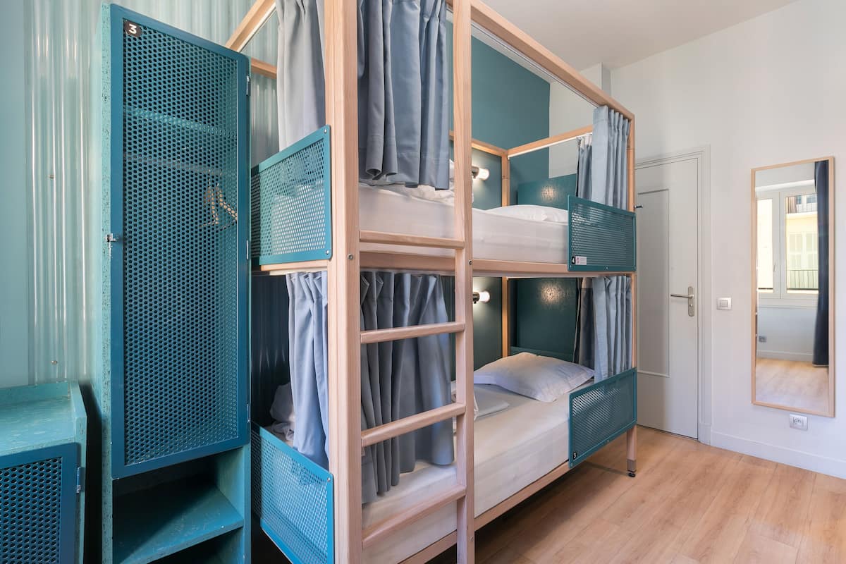 Une chambre avec un lit superposé, une armoire en métal et un miroir.