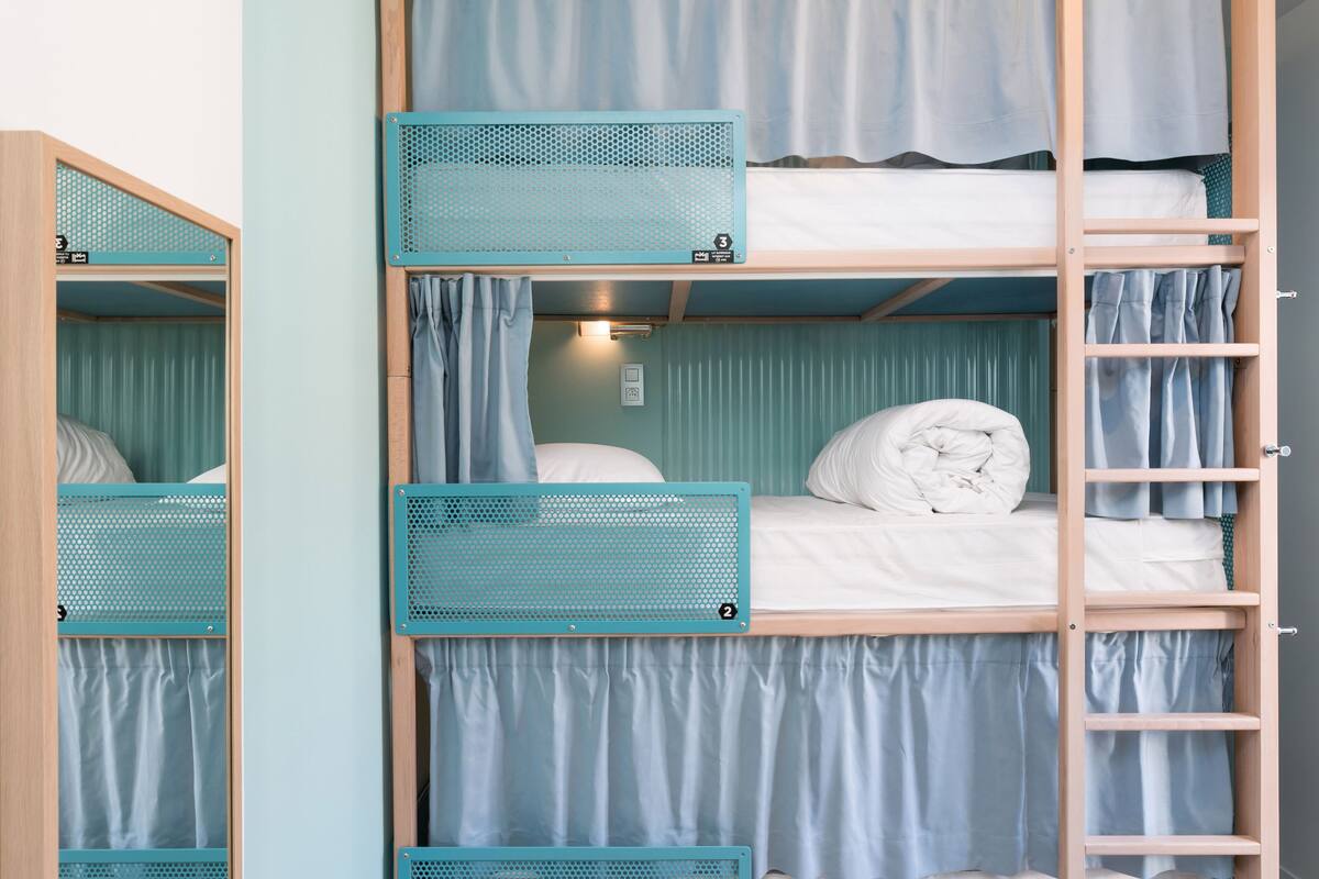 Une chambre avec un lit superposé, une échelle, des rideaux et une petite étagère.