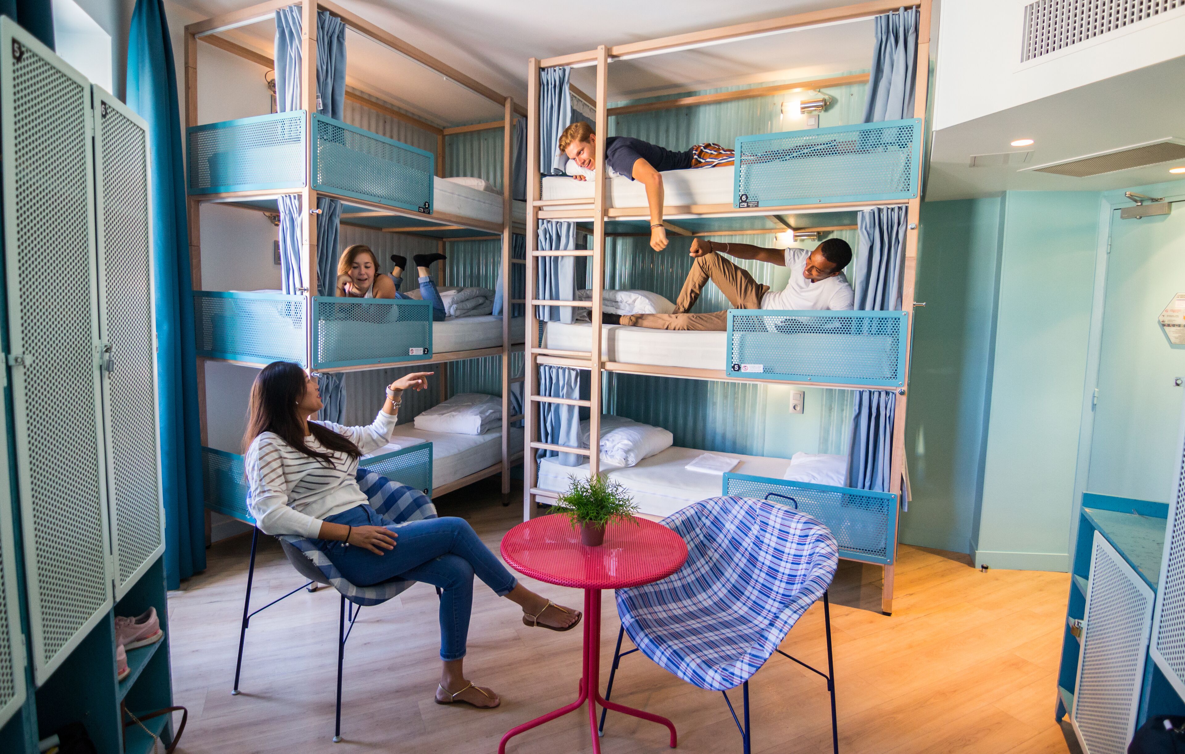A room with bunk beds, a small round table with a plant, and a chair.