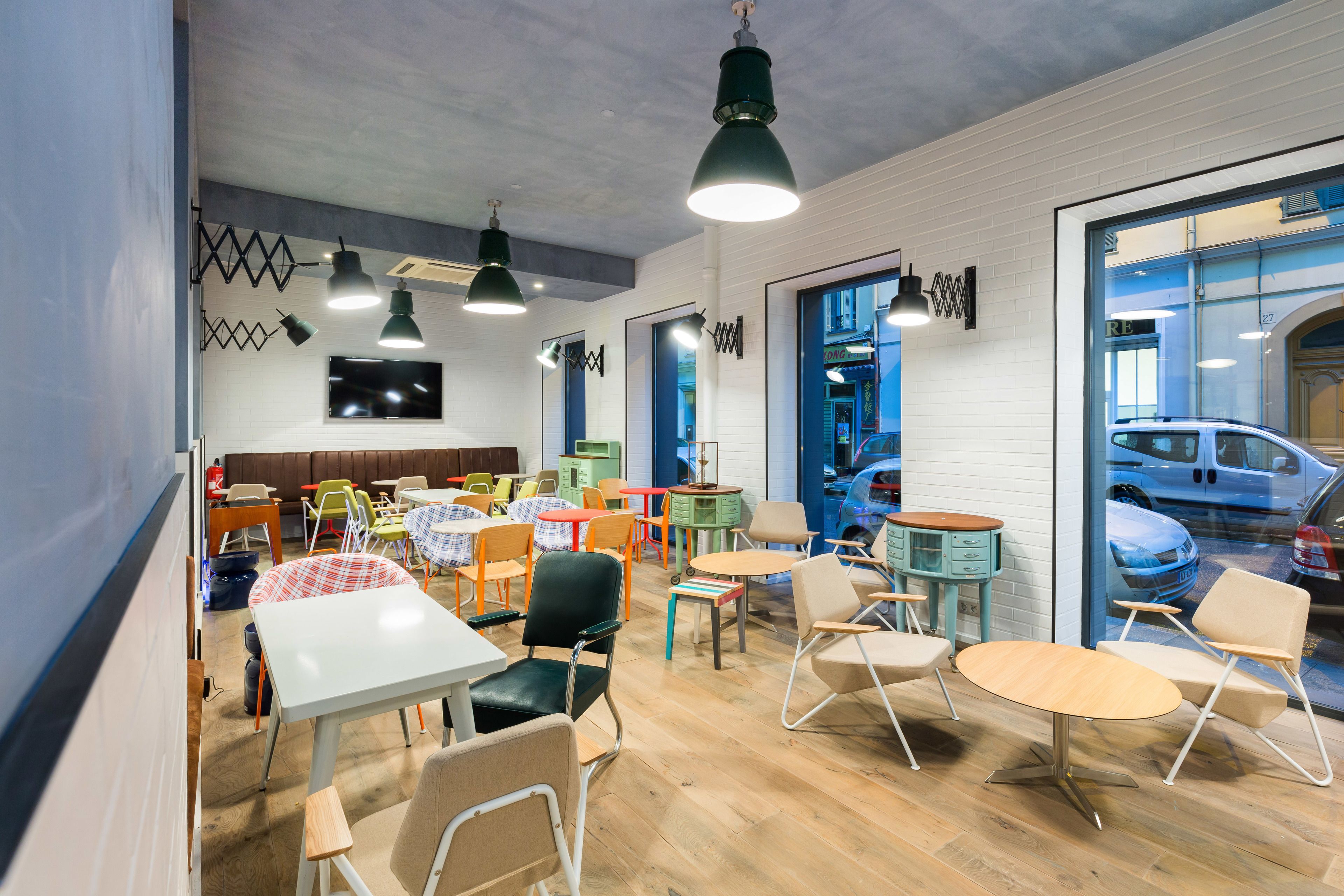 A modern cafe with multiple seating areas, including tables and chairs, and a large window offering a view of parked cars.