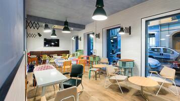 A modern cafe with multiple seating areas, including tables and chairs, and a large window offering a view of parked cars.