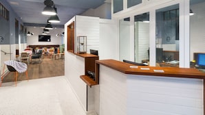 Ein moderner Empfangsbereich mit einem Holzbüro, einer Sitzecke mit Tischen und Stühlen sowie einem großen Fenster mit Blick ins Innere.