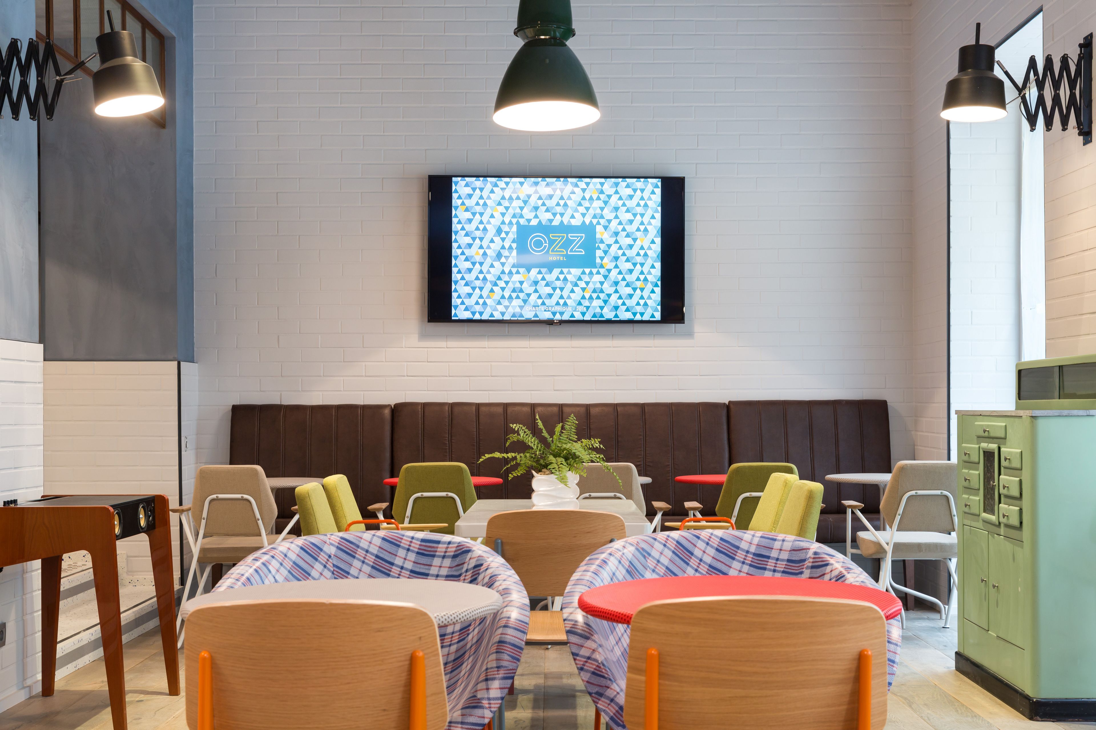 Un restaurant moderne doté d’une grande table conviviale, de banquettes et d’un écran de télévision affichant le nom de l’établissement.
