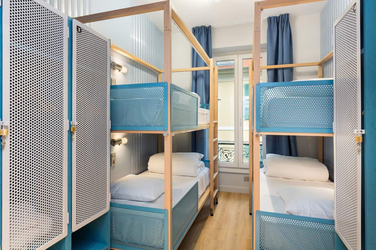 Une chambre avec des lits superposés, un plancher en bois et une fenêtre avec des rideaux.