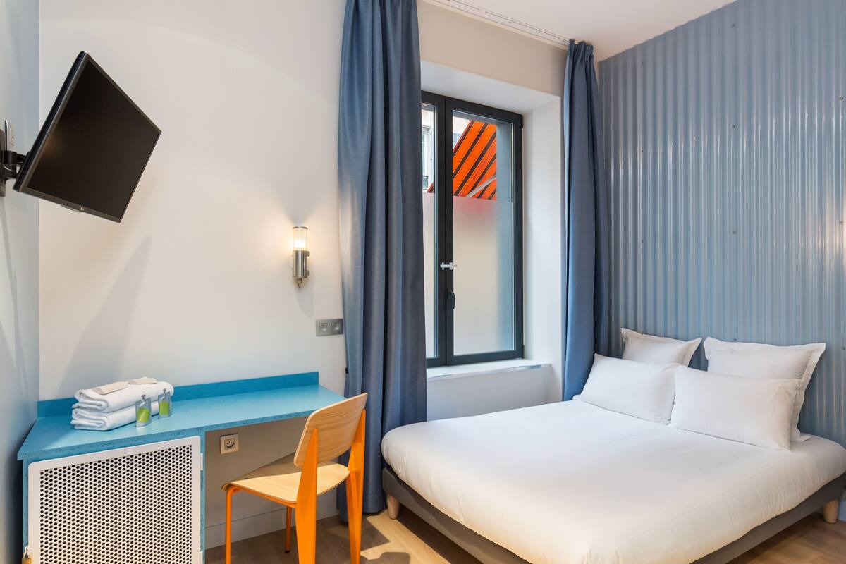 Une chambre d’hôtel équipée d’un lit, d’un bureau, d’une chaise, d’un téléviseur à écran plat et d’une fenêtre avec des rideaux.
