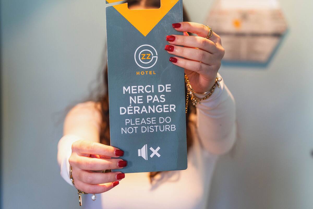Une personne tenant une pancarte ornée du logo d’un hôtel et portant un message en français et en anglais.