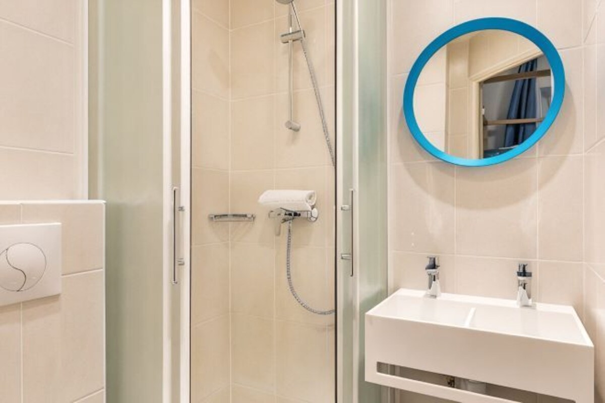 Une salle de bain avec une douche à parois de verre, un lavabo blanc et un miroir rond doté d’un cadre bleu.