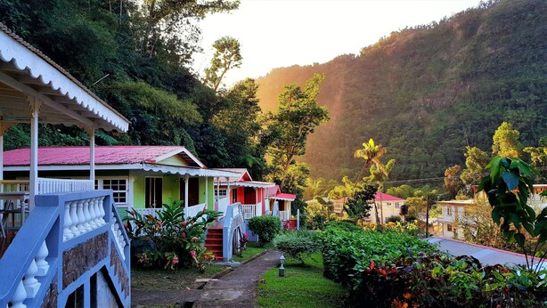 A row of two-story houses with red roofs, surrounded by lush greenery and hills in the background. - Chez Ophelia Cottage Apartments (Roseau)
