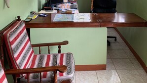 A room with a desk, a chair, a computer, a window with curtains, and a ceiling fan. - Chez Ophelia Cottage Apartments (Roseau)
