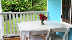 A white table with a vase of red flowers on a balcony with white railings. - Chez Ophelia Cottage Apartments (Roseau)