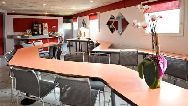 Een restaurant met een lange balie, meerdere tafels en stoelen. Op de balie staat een decoratieve vaas met bloemen.