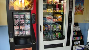 Een automaat met verschillende drankjes, waaronder Nescafe en andere opties, en een afdeling voor snacks zoals chips en snoep.