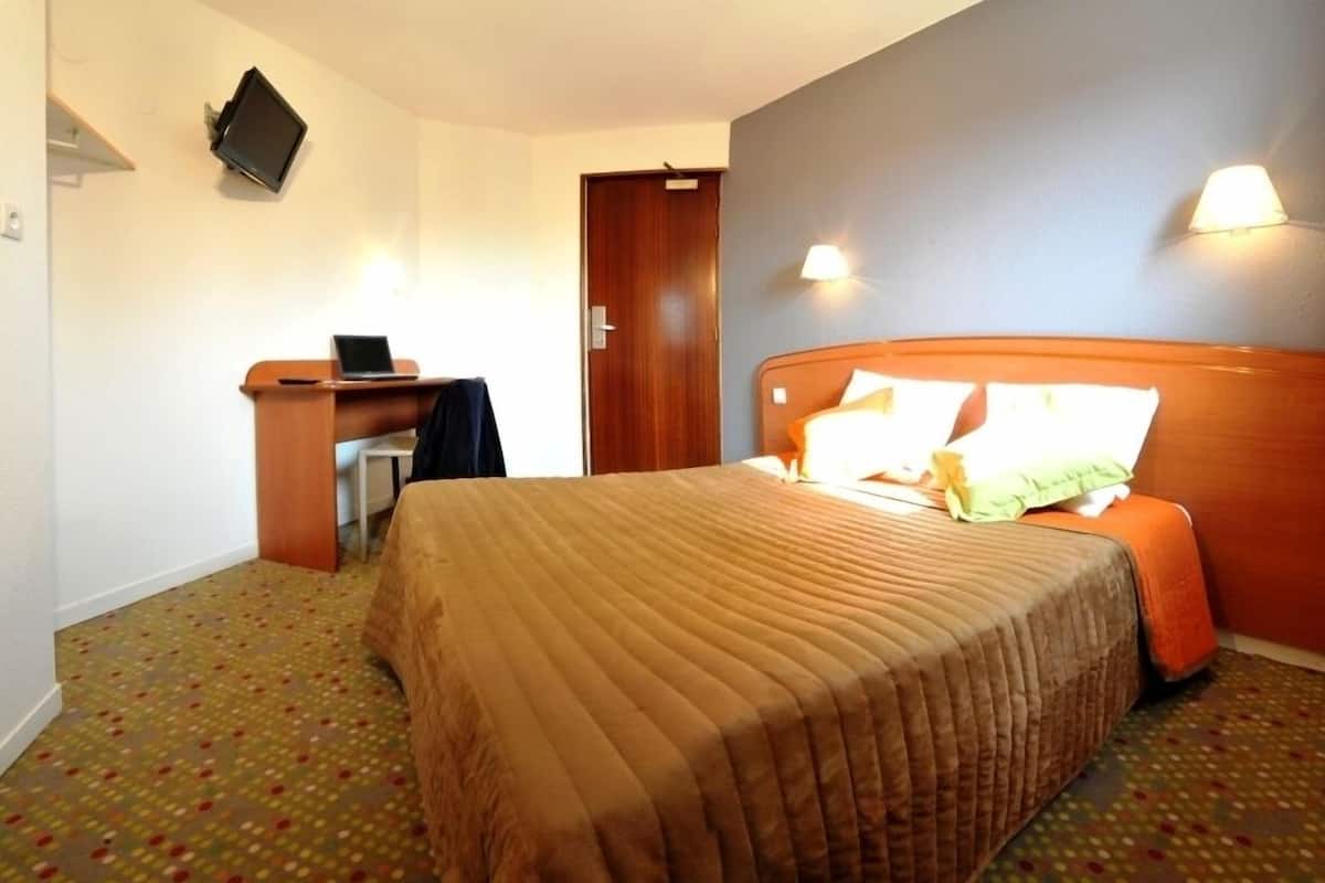 Een hotelkamer met een bed, een bureau, een laptop en een aan de muur bevestigde televisie.
