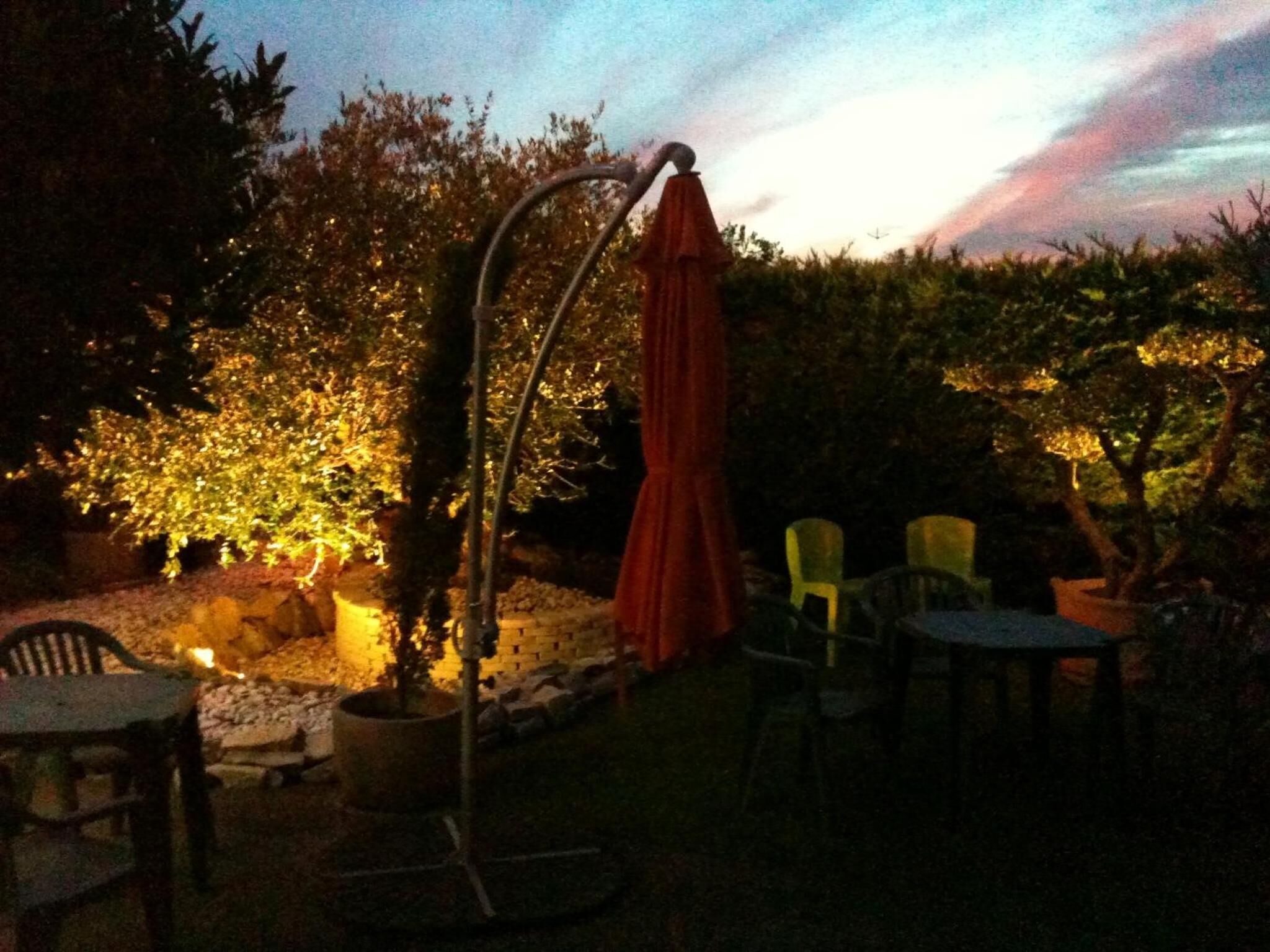 Un área de patio al aire libre con una sombrilla metálica, sillas y plantas en macetas.