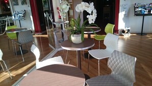 Ein modernes Interieur mit runden Tischen und weiß gepolsterten Stühlen, einer Topfpflanzen-Orchidee und einem Bücherregal mit Büchern und Zeitschriften.
