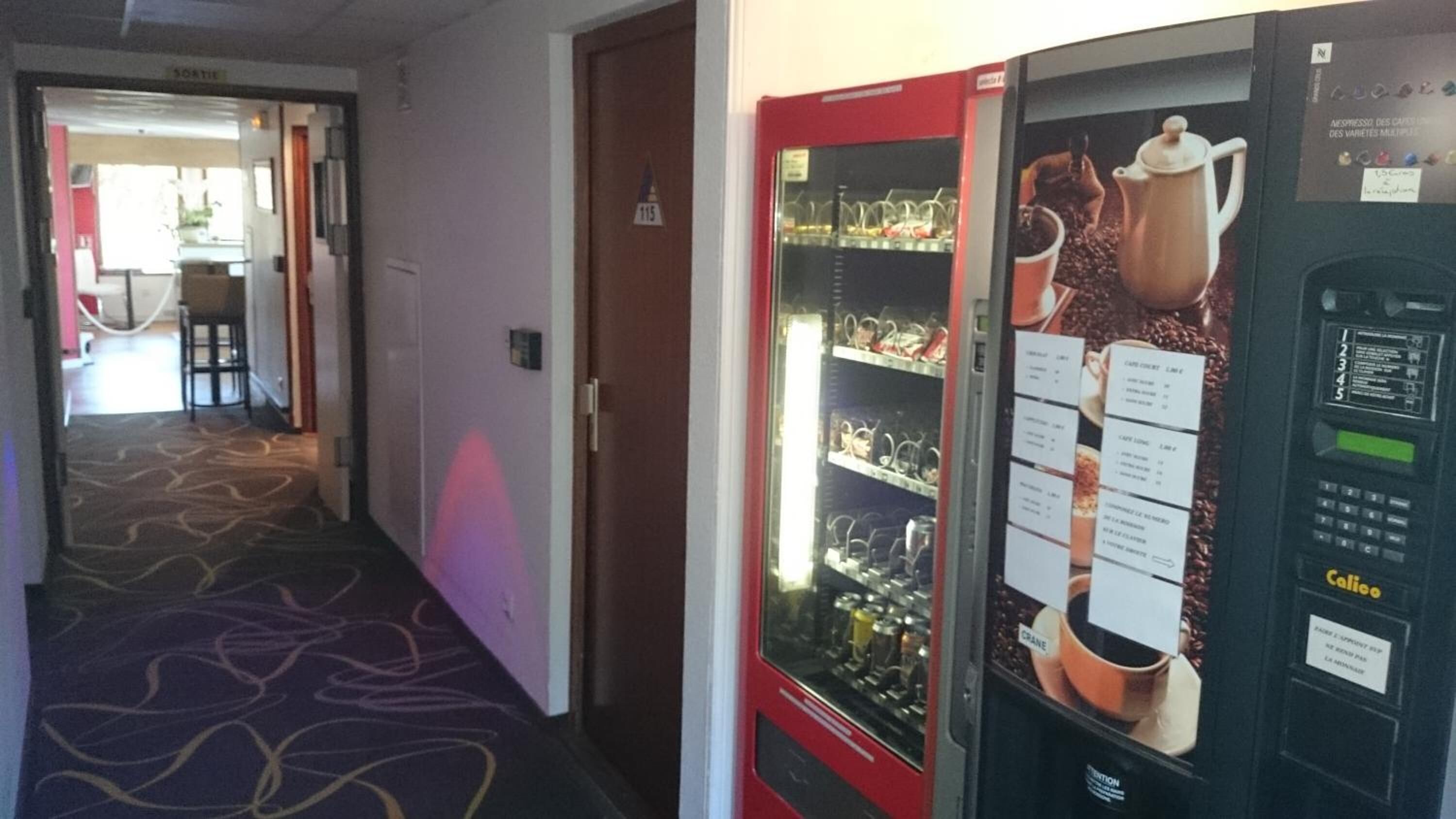 Un couloir avec un distributeur de café et un espace détente avec des sièges.
