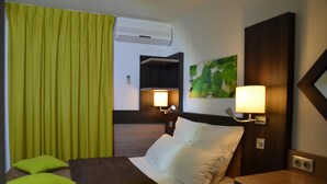 Ein Hotelzimmer mit Bett, grünen Vorhängen, einer Wand-Klimaanlage und zwei Nachttischlampen.