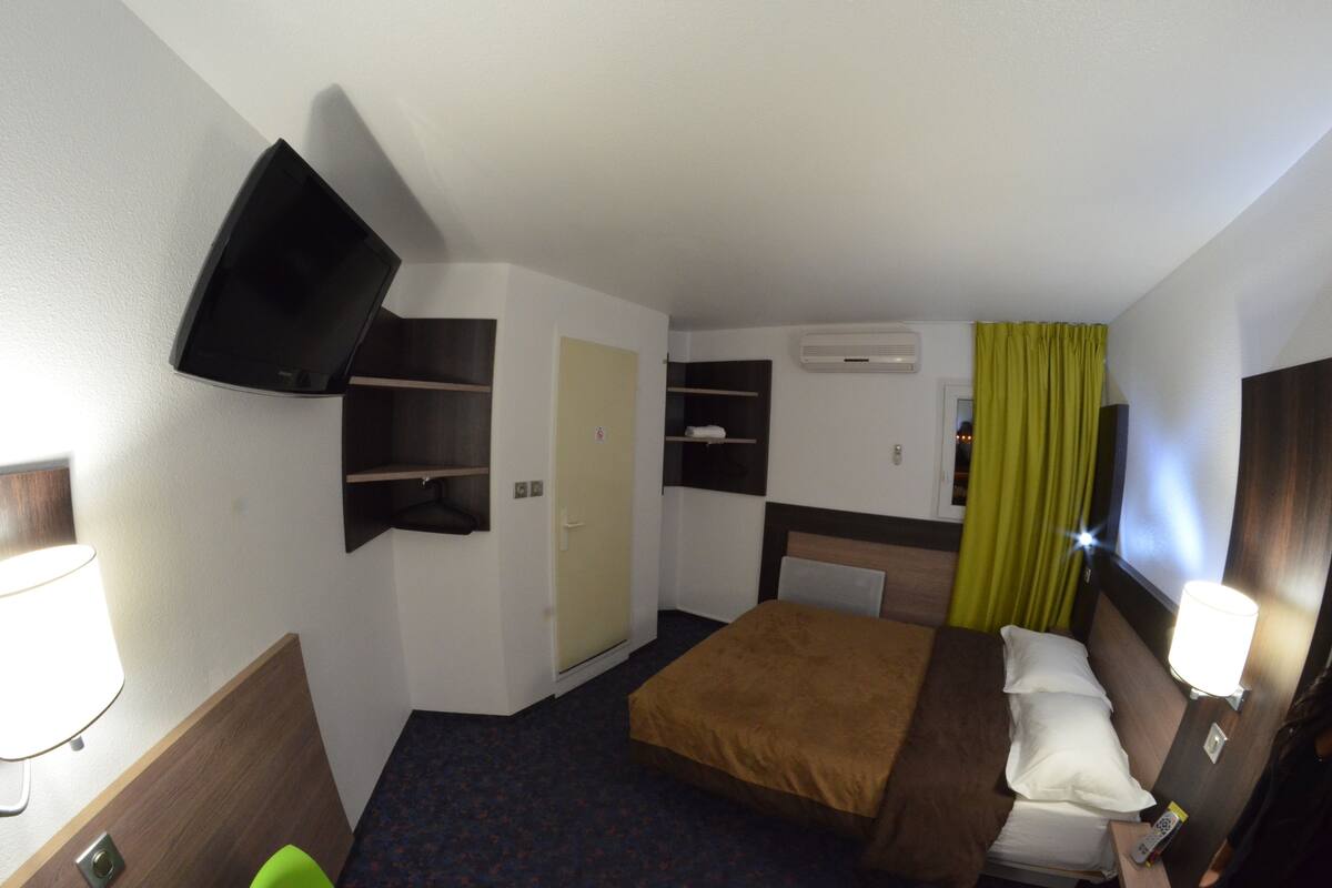 A compact hotel room with a bed, a television mounted on the wall, a wardrobe, and a small shelf unit.