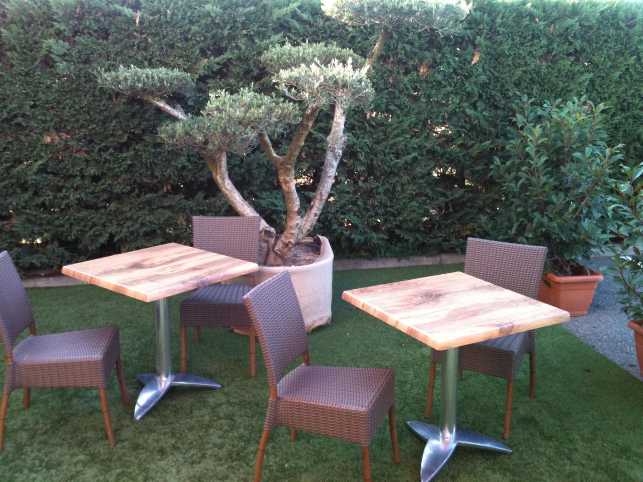 An outdoor seating area with four square wooden tables and wicker chairs.