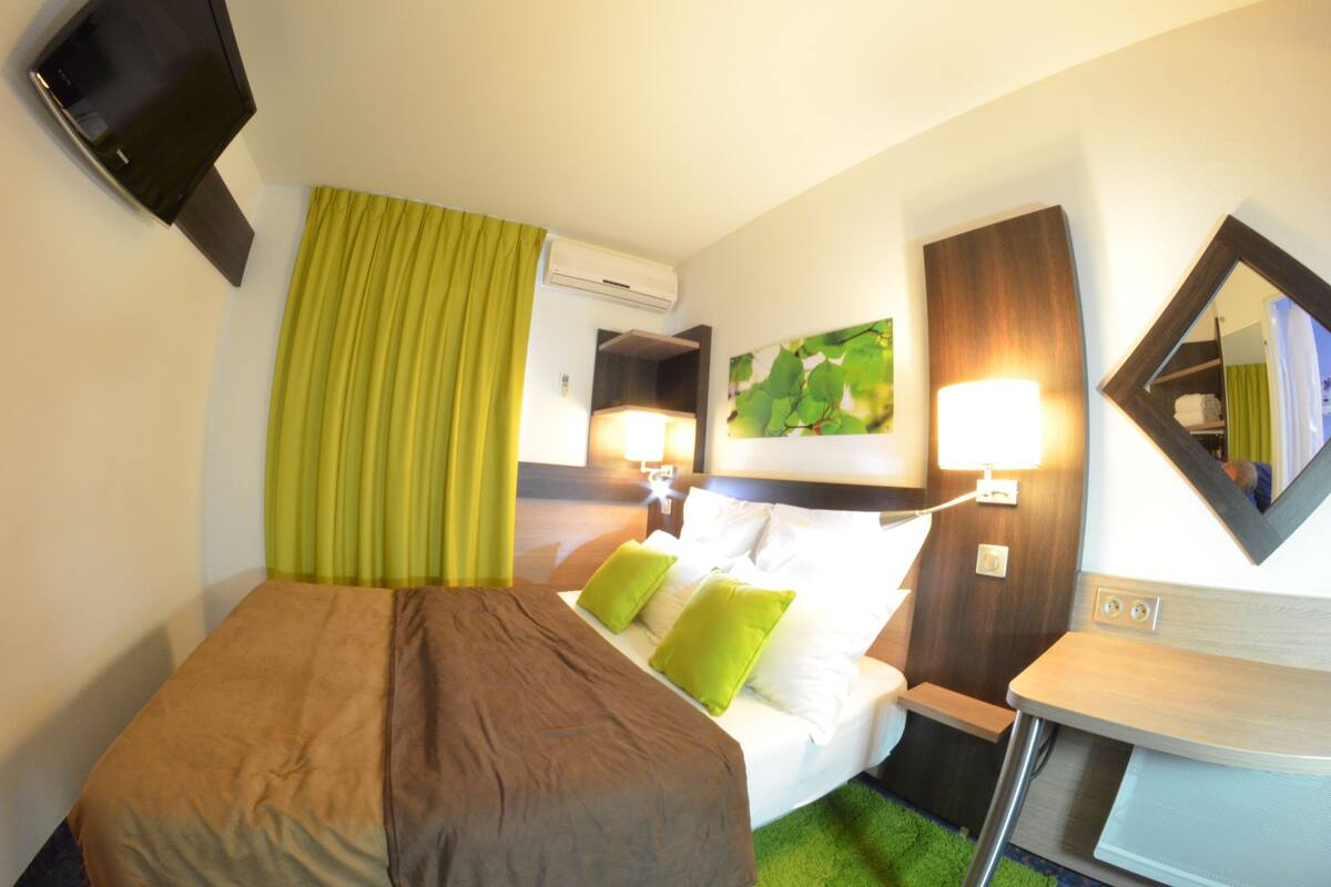 A hotel room with a bed, bedside table, and a mirror.