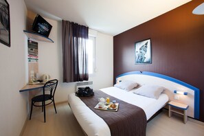 Een hotelkamer met een bed, een bureau, een stoel, een televisie, een raam met gordijnen, een nachtkastje en een dienblad met ontbijtartikelen.