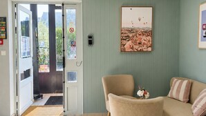 A reception area with a door, a framed landscape painting, a sofa, and a chair. - Hotel Dom le Breton Nantes Beaujoire - Porte de Sainte Luce (Sainte-Luce-sur-Loire)